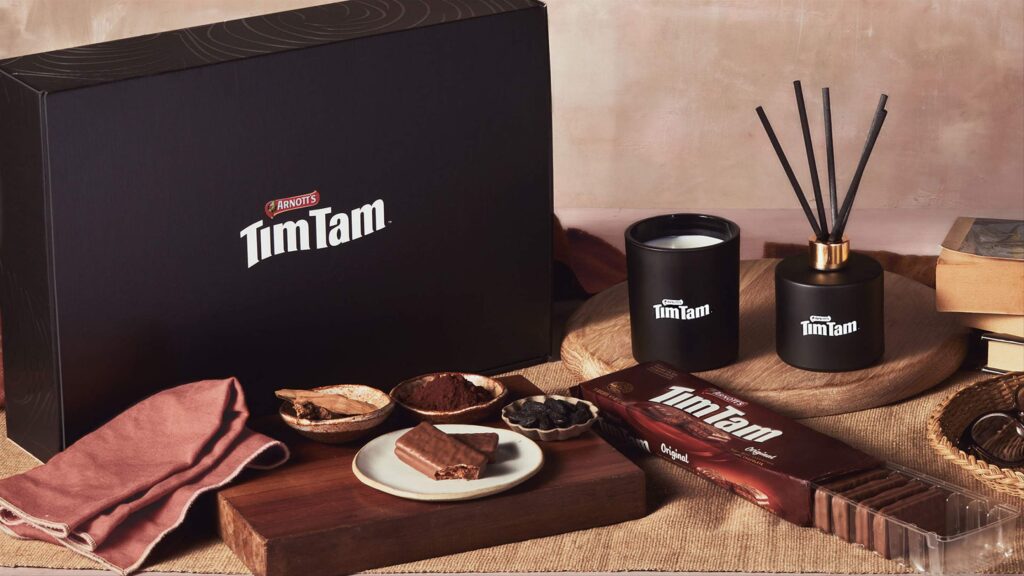 Tim Tam gift set featuring Arnott’s Tim Tam biscuits, a black branded candle, reed diffuser, and chocolate-inspired ingredients, styled with wooden trays and rustic accents.
